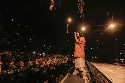 Billie Eilish śpiewa na koncercie przed rozentuzjazmowanym tłumem z telefonami w górze.