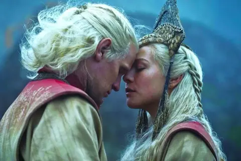 Ród smoka sezon 2: Daemon i Rhaenyra w intymnym uścisku, ich czoła się stykają, a w tle widać mglisty krajobraz.