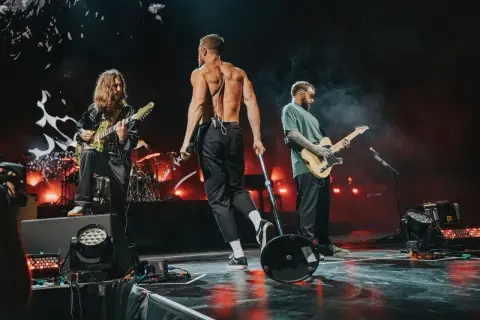 Imagine Dragons na koncercie w Polsce: wokalista bez koszulki, gitarzyści grający na scenie.