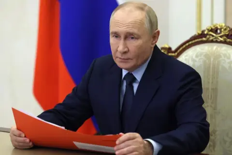 Władimir Putin w garniturze, z rosyjską flagą w tle, trzyma teczkę.