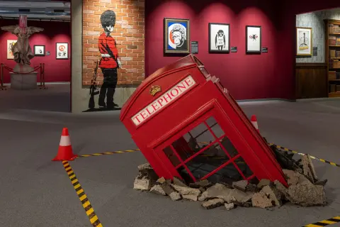 Wystawa Banksy Warszawa: przewrócona budka telefoniczna, mural z żołnierzem i prace artysty.