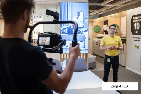 Operator kamery nagrywa pracownika IKEA w sklepie, na ekranie w tle reklama materaca.
