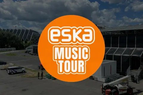 Pomarańczowe koło z napisem "ESKA MUSIC TOUR" na tle sceny koncertowej i parkingu.