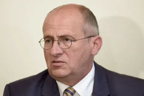 Portret starszego mężczyzny w okularach i garniturze.