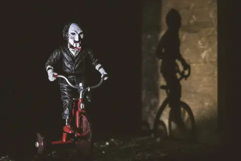Figurka Billy'ego z horroru 2023 na czerwonym rowerku trójkołowym, rzucająca złowieszczy cień.