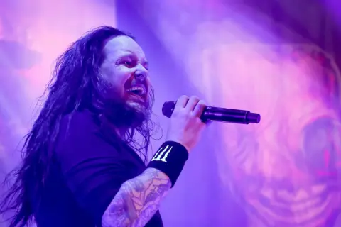 Jonathan Davis z zespołu Korn śpiewający do mikrofonu na fioletowej scenie.