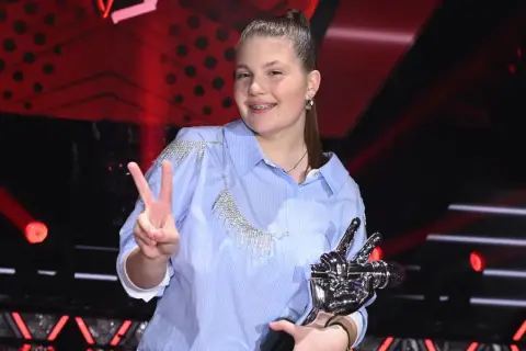 Dziewczynka w błękitnej koszuli z kryształkami, trzymająca statuetkę i pokazująca znak V.