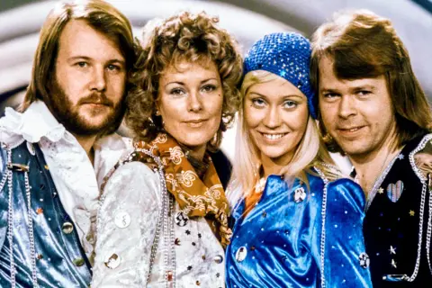 Zespół ABBA w strojach scenicznych, uśmiechnięci, patrzą w obiektyw.