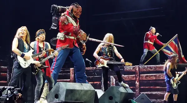 Zespół Iron Maiden na scenie, w tym Eddie w czerwonym mundurze, grający na gitarach i z flagą Wielkiej Brytanii.
