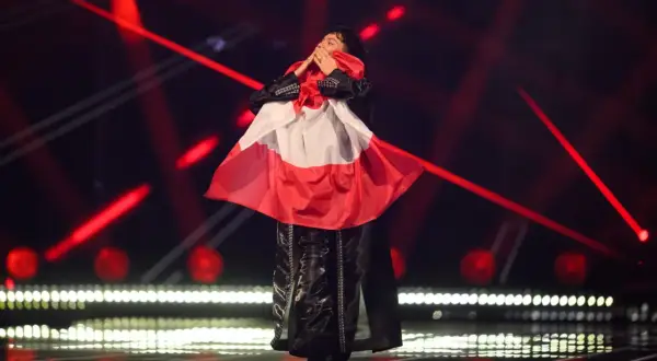 Eurowizja zwycięzcy: artysta w czarnym stroju z biało-czerwoną flagą na scenie, otoczony czerwonymi światłami.