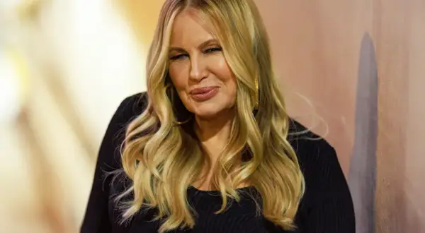 Uśmiechnięta mama Stiflera z blond włosami, w czarnej bluzce, z dużymi złotymi kolczykami.