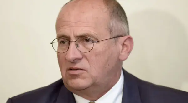 Portret starszego mężczyzny w okularach i garniturze.