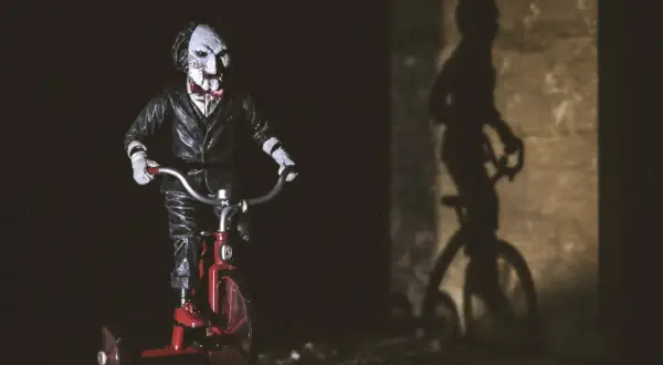 Figurka Billy'ego z horroru 2023 na czerwonym rowerku trójkołowym, rzucająca złowieszczy cień.