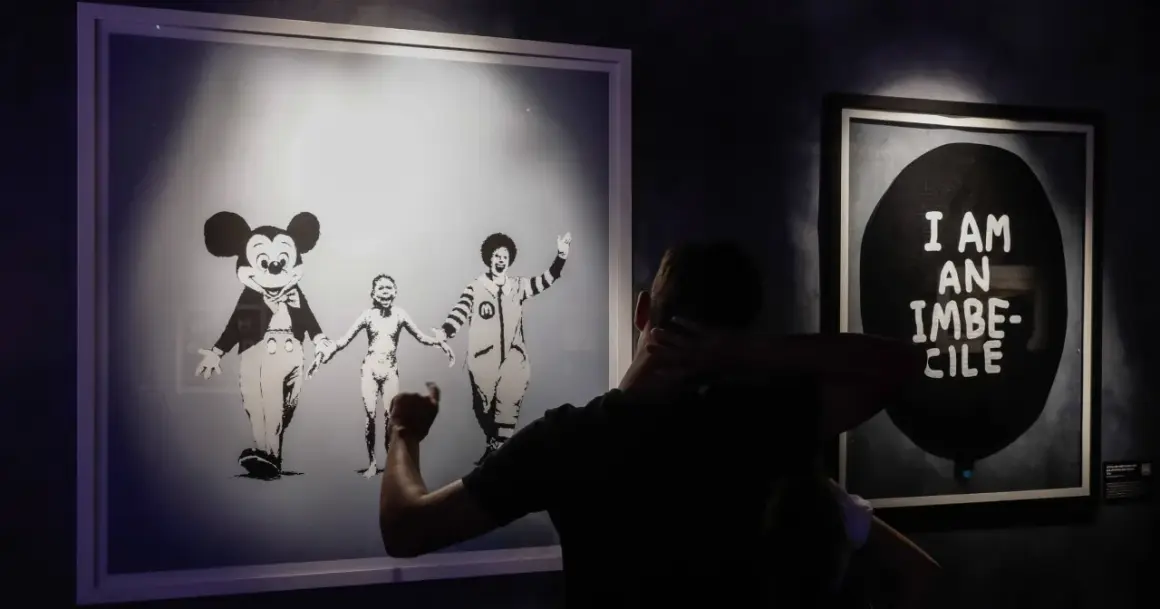 Wystawa "Banksy zdemaskowany" prezentuje dzieła artysty, w tym obraz z postaciami Myszki Miki i Ronalda McDonalda trzymających się za ręce.