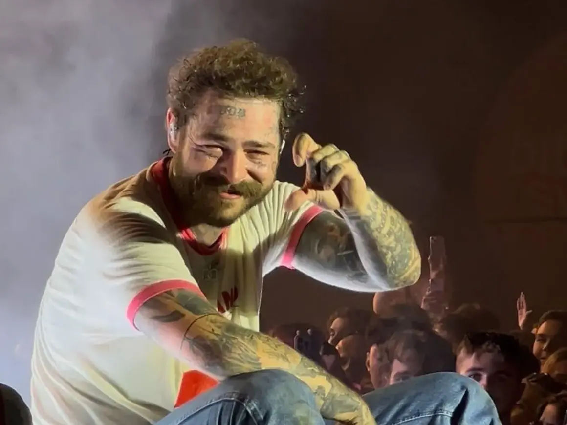 Post Malone na koncercie, uśmiecha się i pokazuje gest ręką.