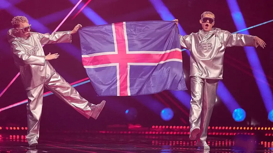 Dwóch artystów w srebrnych strojach prezentuje flagę Islandii na scenie Eurowizji.