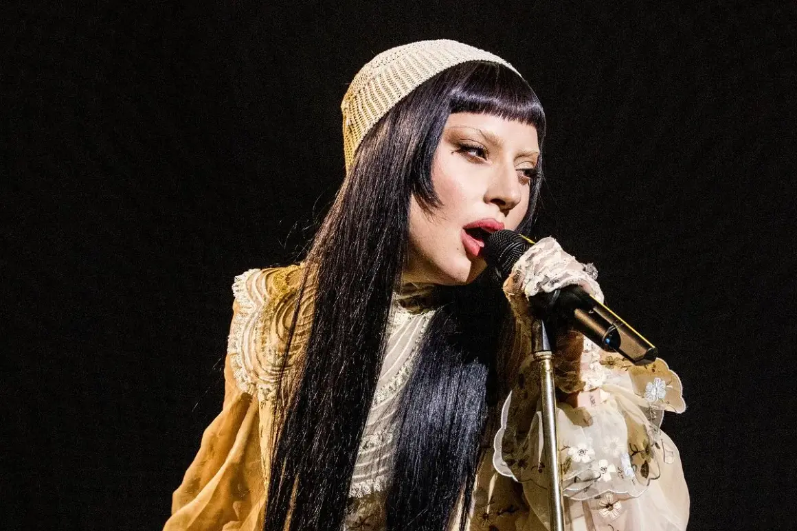Lady Gaga w beżowym nakryciu głowy i ozdobnej sukni śpiewa do mikrofonu.
