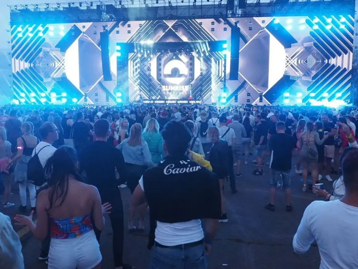 Tłum ludzi na festiwalu Sunrise w Kołobrzegu, podziwiający ogromną scenę z efektami świetlnymi.