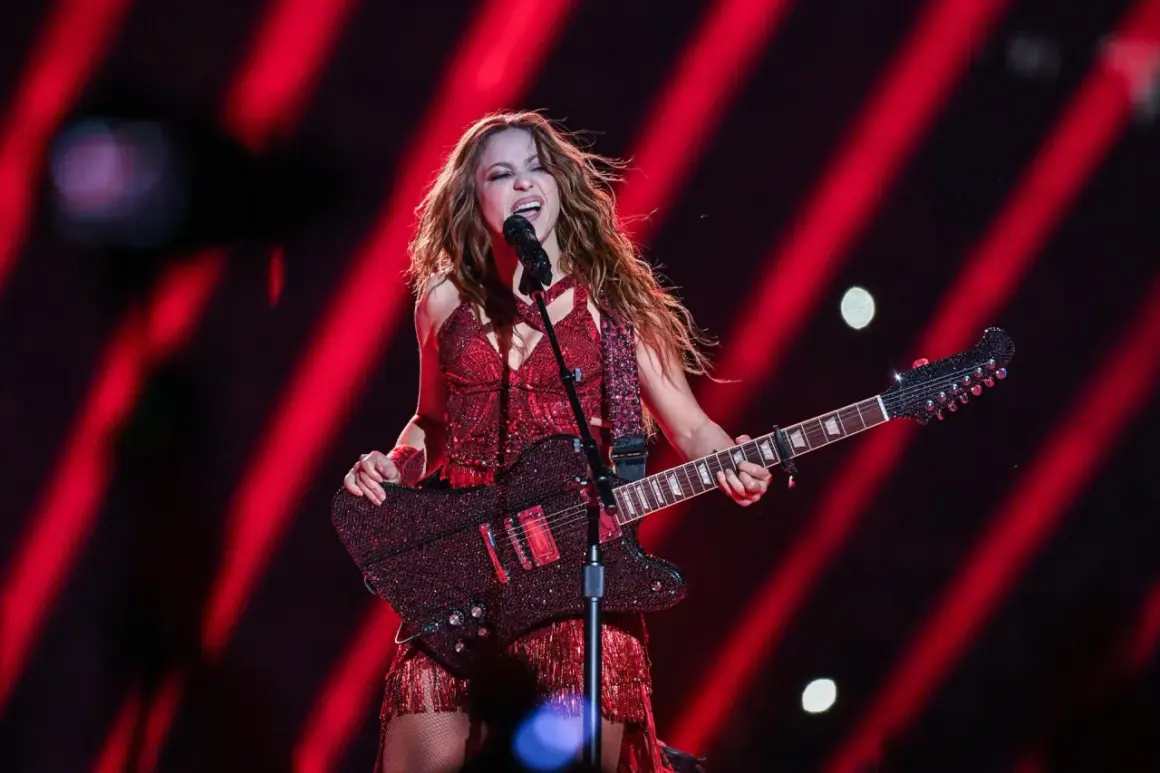Shakira w czerwonym stroju śpiewa i gra na gitarze na tle czerwonych świateł.