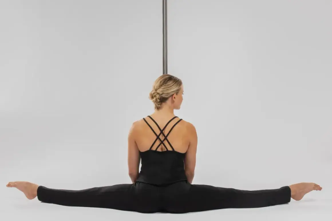 Kobieta w czarnym stroju siedzi w szpagacie przy rurze do pole dance.