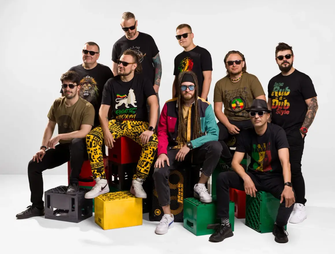 Dziewięciu mężczyzn w okularach przeciwsłonecznych, ubranych w koszulki z motywami reggae, siedzi na skrzynkach po napojach.