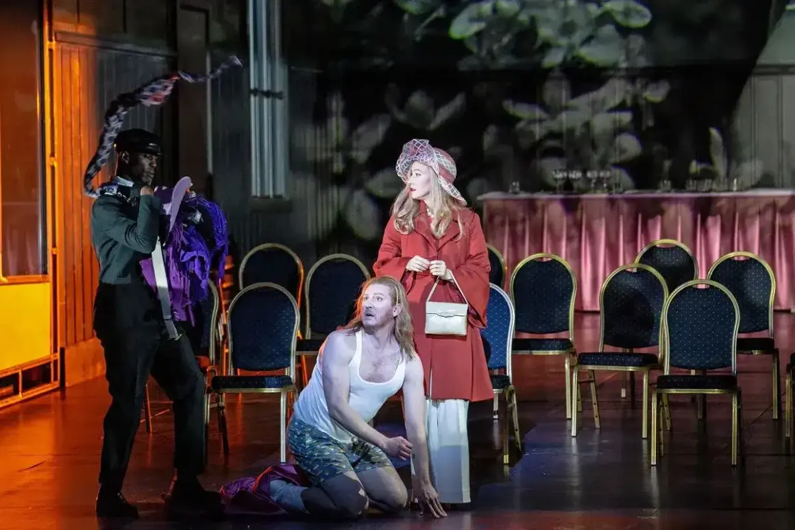 Aktorzy na scenie operetki, mężczyzna klęczy, kobieta stoi, trzeci mężczyzna trzyma kostium.