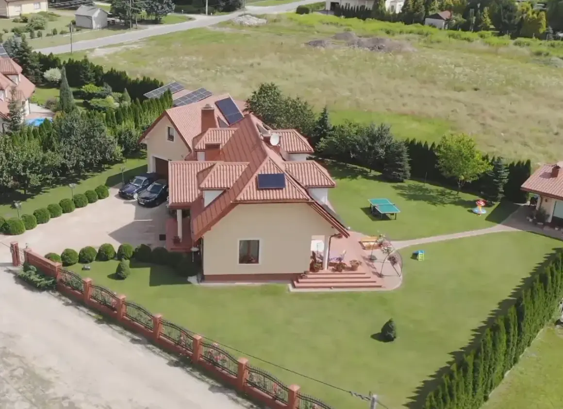 Piękny dom z ogrodem, gdzie mieszka Skolim. Widać panele słoneczne, dwa samochody i plac zabaw.
