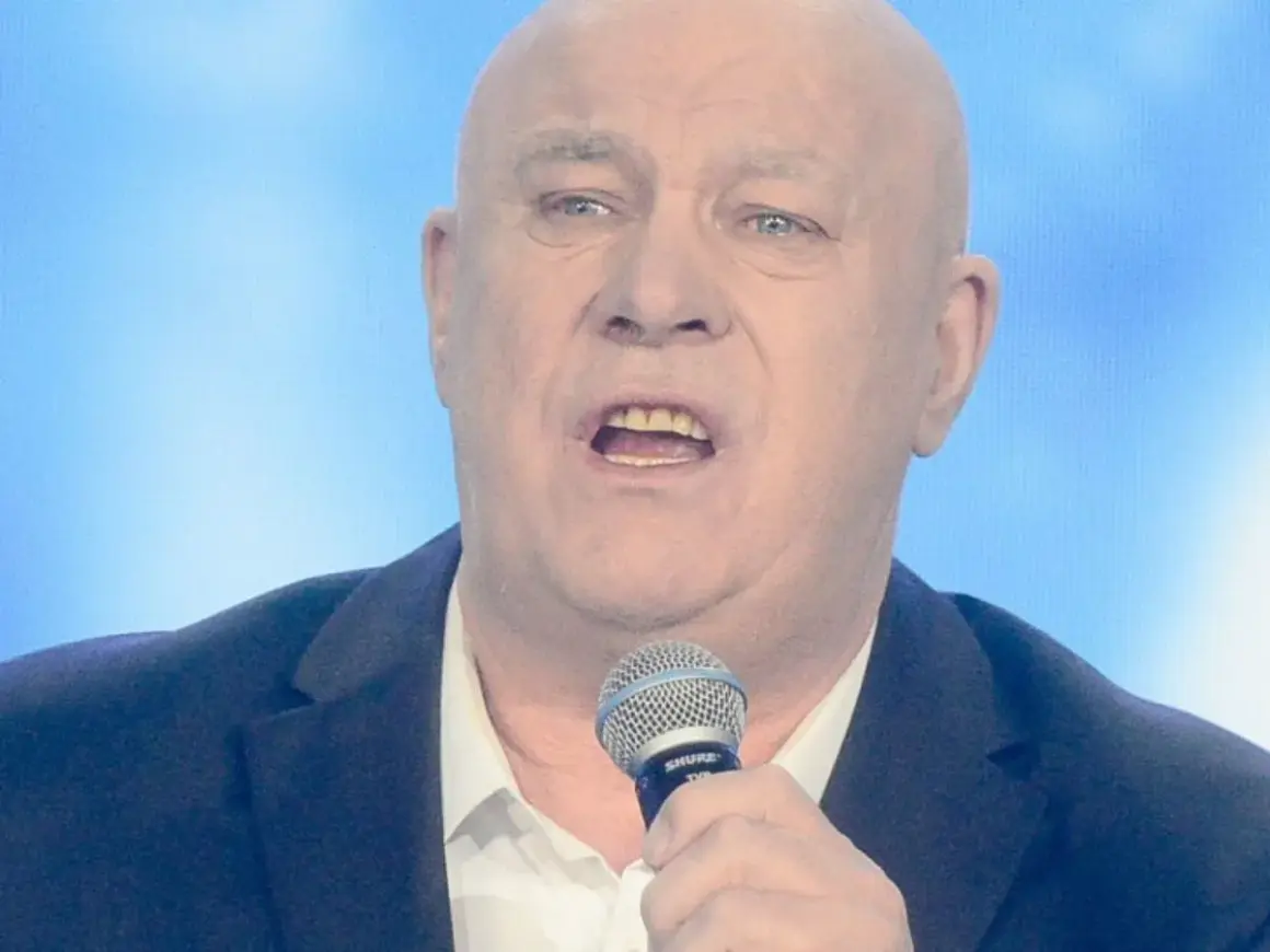 Ryszard Rynkowski śpiewa do mikrofonu, ubrany w marynarkę i białą koszulę.
