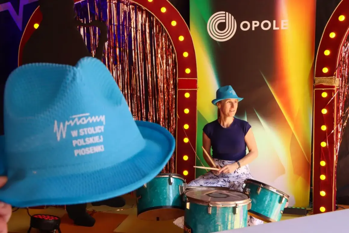 Kobieta w niebieskim kapeluszu gra na perkusji przed sceną z napisem "Opole".