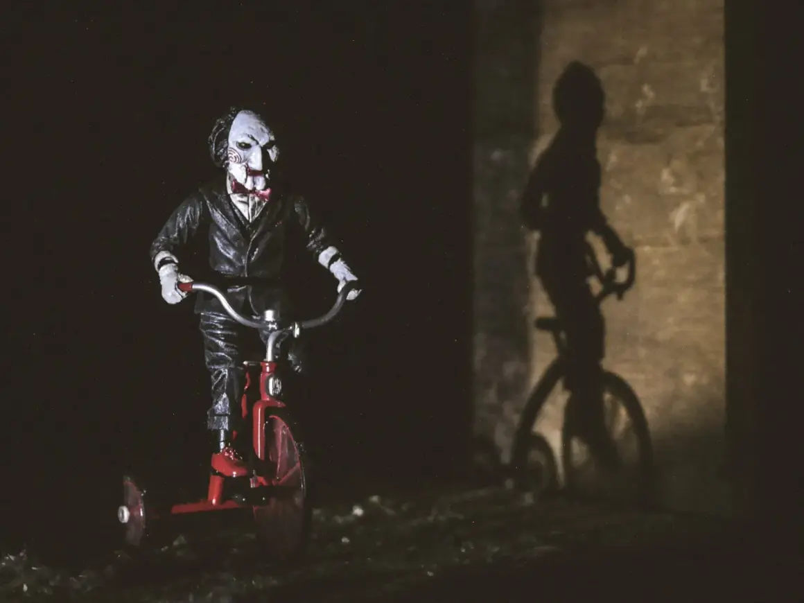 Figurka Billy'ego z horroru 2023 na czerwonym rowerku trójkołowym, rzucająca złowieszczy cień.