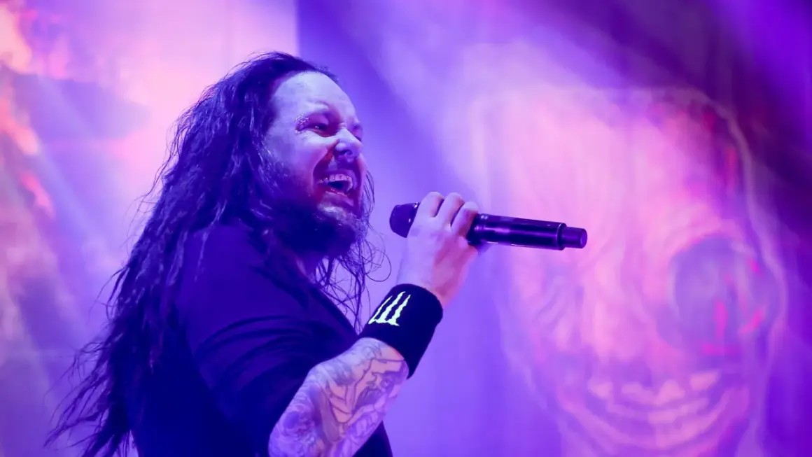Jonathan Davis z zespołu Korn śpiewający do mikrofonu na fioletowej scenie.