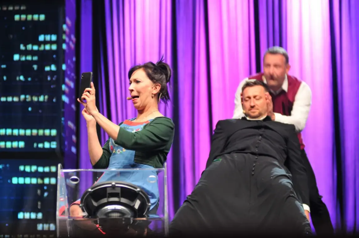 Trzech aktorów na scenie: kobieta robi selfie, mężczyzna w sutannie i drugi mężczyzna za nim.