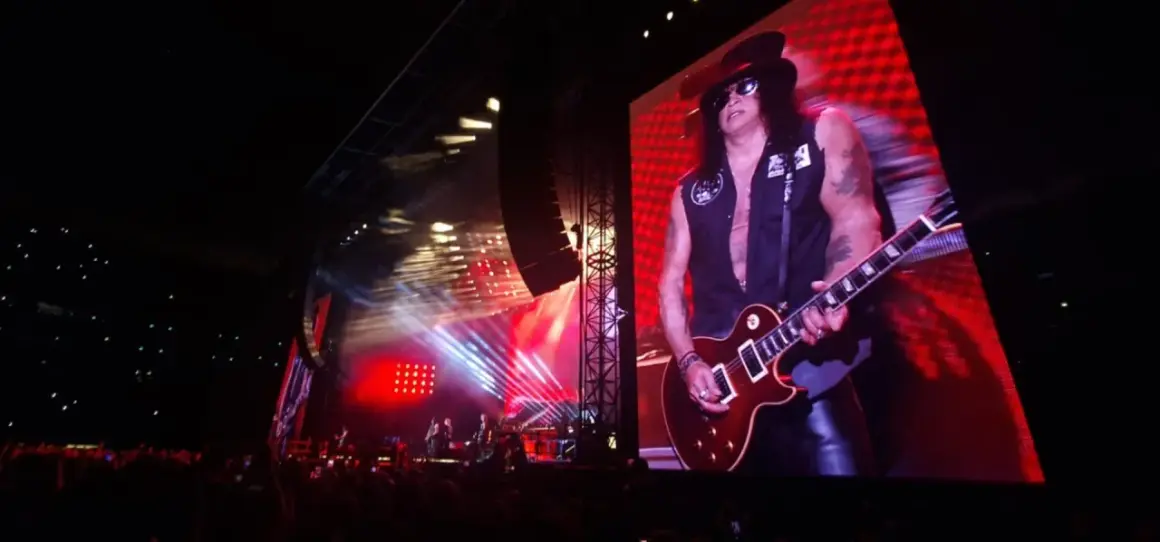 Slash z Guns N' Roses gra na gitarze na wielkim ekranie podczas koncertu.
