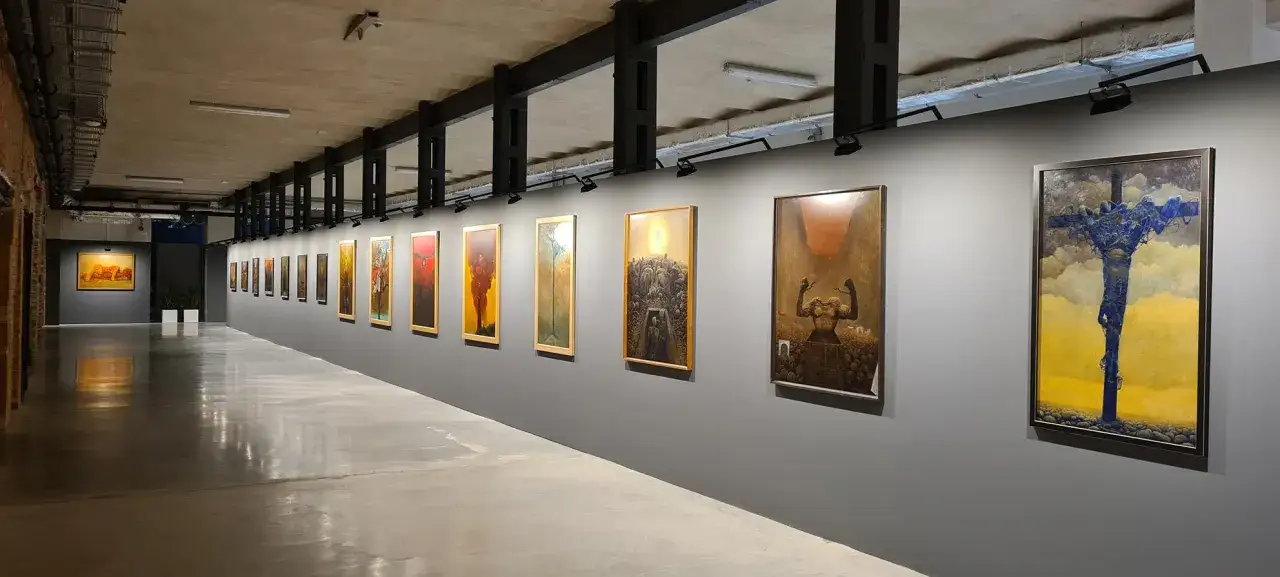 Wystawa Beksińskiego w Warszawie. Długi korytarz galerii z rzędem jego mrocznych, surrealistycznych obrazów.
