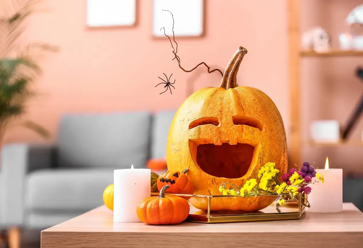 Wesoła dynia z wyciętą buzią i pająkiem na gałązce, otoczona mniejszymi dyniami i świecami. Idealna dekoracja, kiedy jest Halloween.