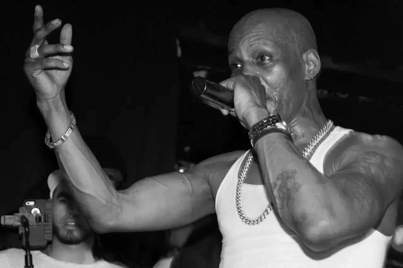 DMX, w białej podkoszulce, z łańcuchem i mikrofonem w dłoni, w emocjonalnym geście na scenie.