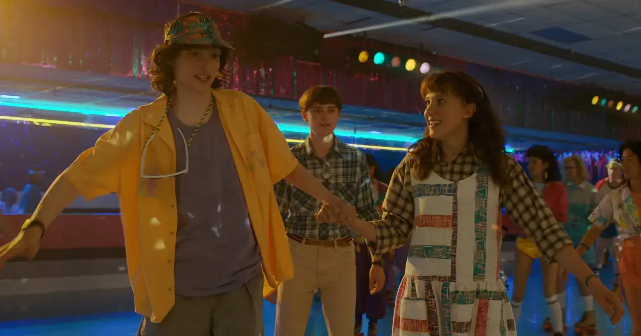 Mike i Eleven z Stranger Things na rolkowisku, trzymając się za ręce.