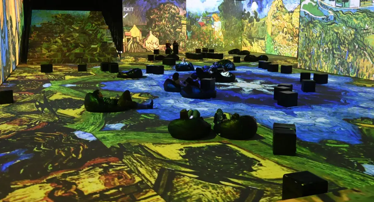Wystawa Van Gogh w Krakowie. Widzowie odpoczywają na pufach, otoczeni projekcjami obrazów artysty.