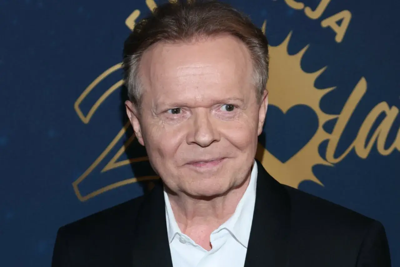 Michał Bajor w czarnym garniturze i białej koszuli, uśmiecha się. W tle złote napisy i serce.