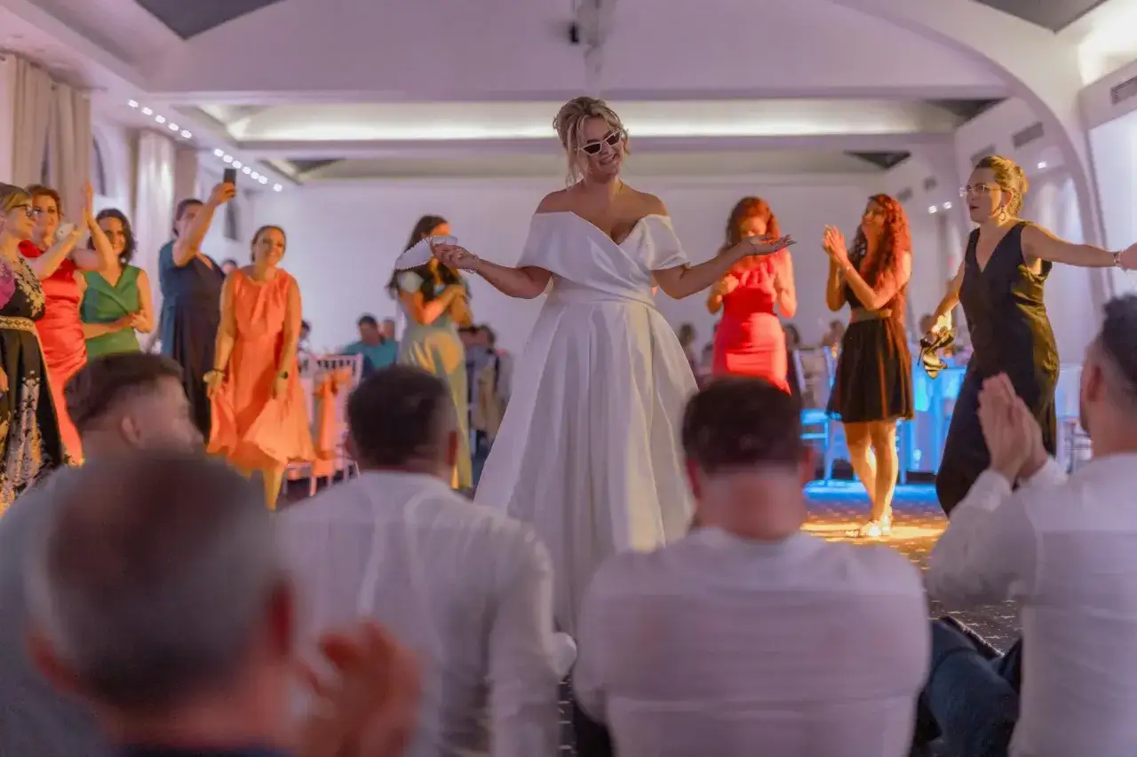 Panna młoda w białej sukni i okularach przeciwsłonecznych tańczy do najpopularniejszych piosenek disco polo, podczas gdy goście klaszczą.