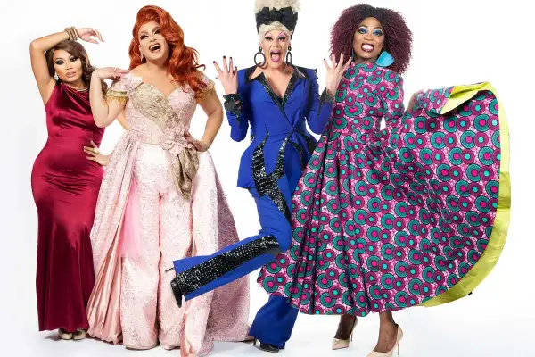 Cztery drag queen w barwnych strojach pozują do zdjęcia na białym tle.