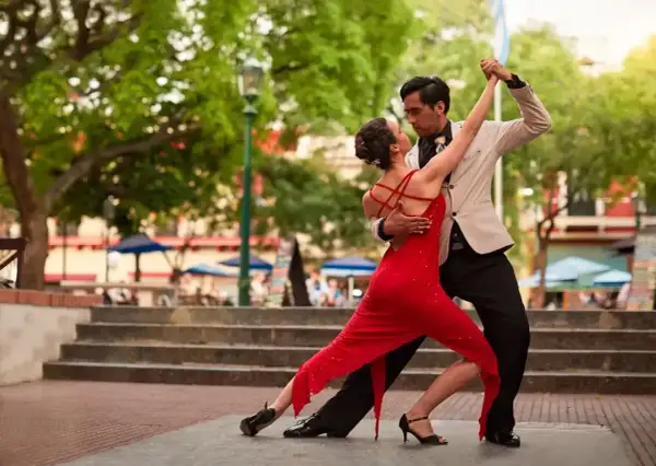 Para tańczy tango na zewnątrz, kobieta w czerwonej sukience, mężczyzna w jasnej marynarce.