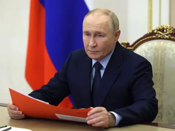 Władimir Putin w garniturze, z rosyjską flagą w tle, trzyma teczkę.